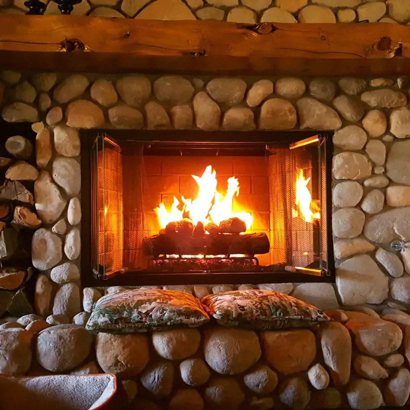 Custom river-stone outdoor fireplace with a timber mantel built by Angel’s Pools